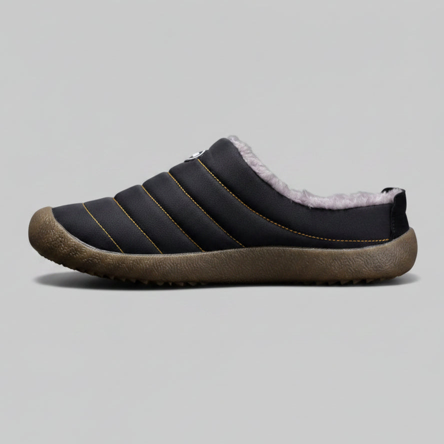 Black slip-on shoe with brown sole on a gray background