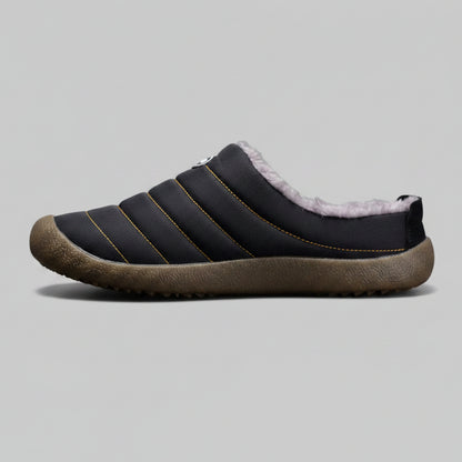 Black slip-on shoe with brown sole on a gray background
