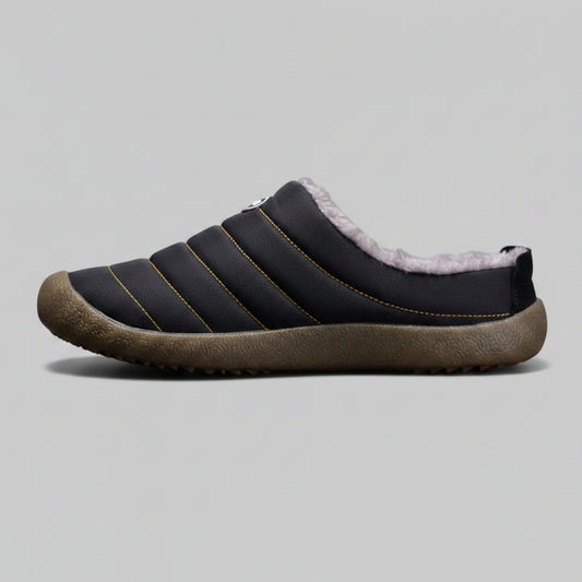 Black slip-on shoe with brown sole on a gray background
