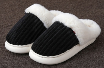 Pair of black and white slippers with fluffy white interior on a brown surface