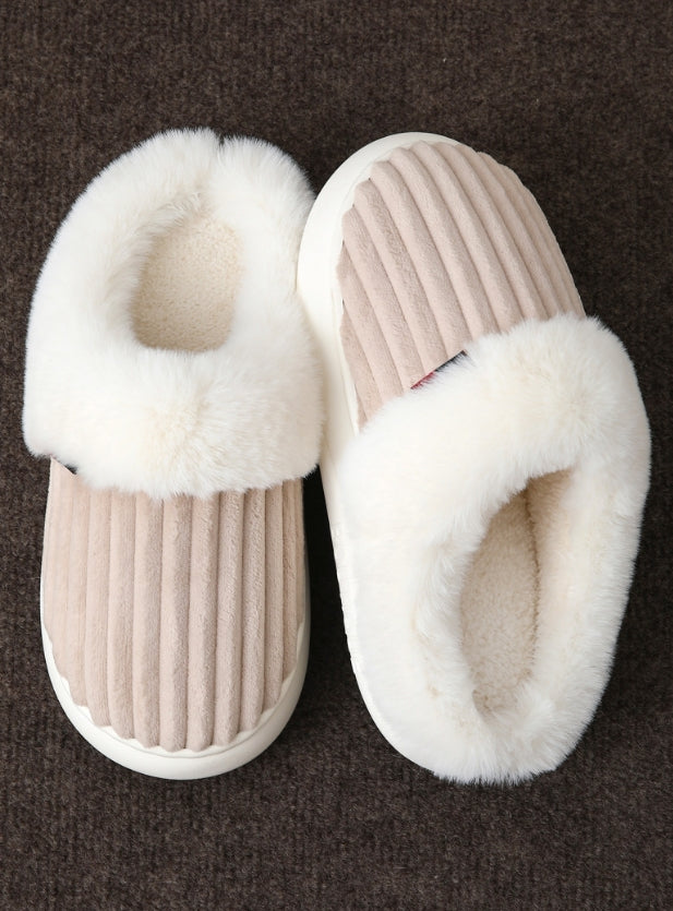 Pair of beige slippers with white fur lining on a brown background