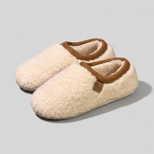 Pair of cream-colored slippers with brown trim on a light gray background